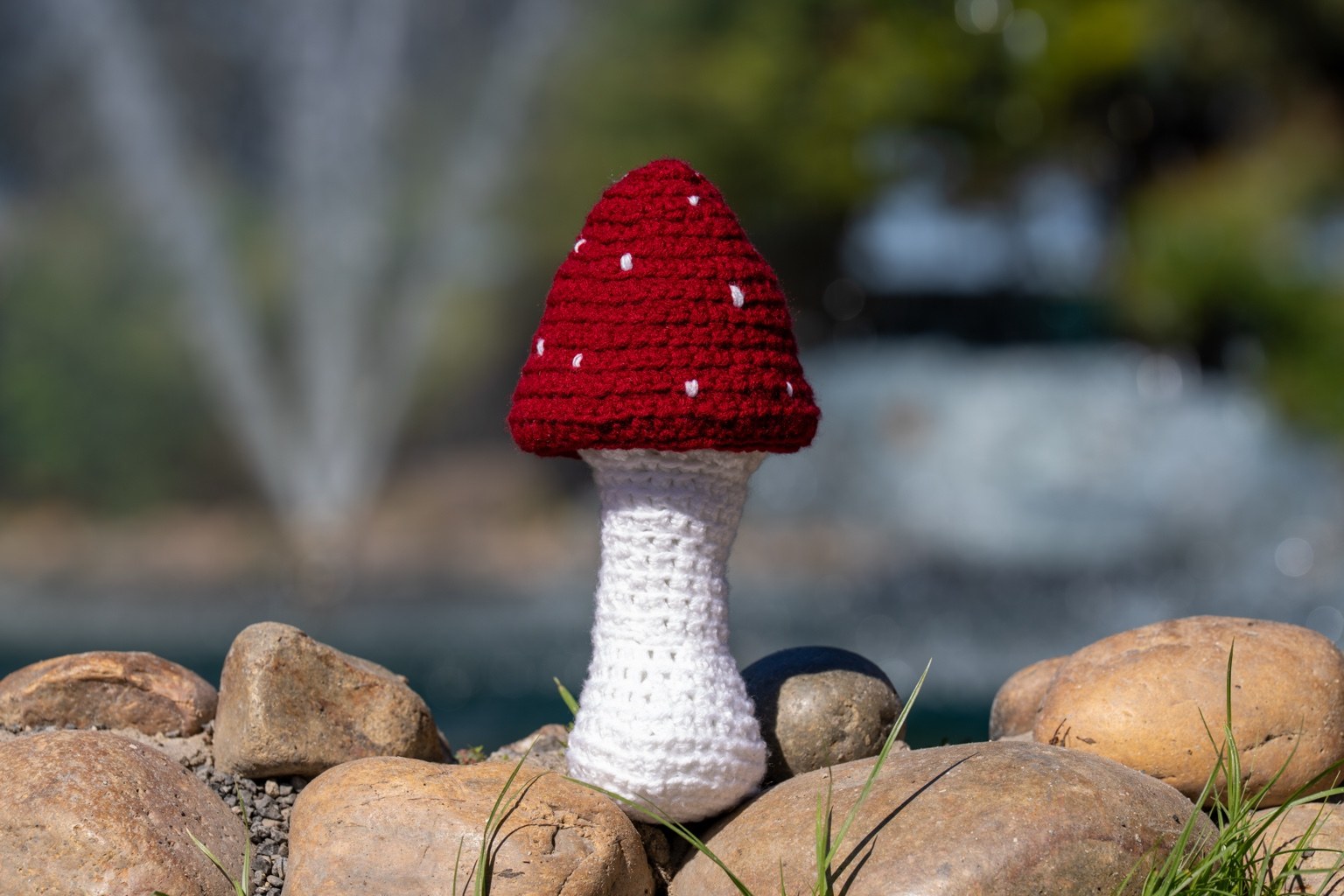 Handmade red and white crochet mushroom displayed on rocks